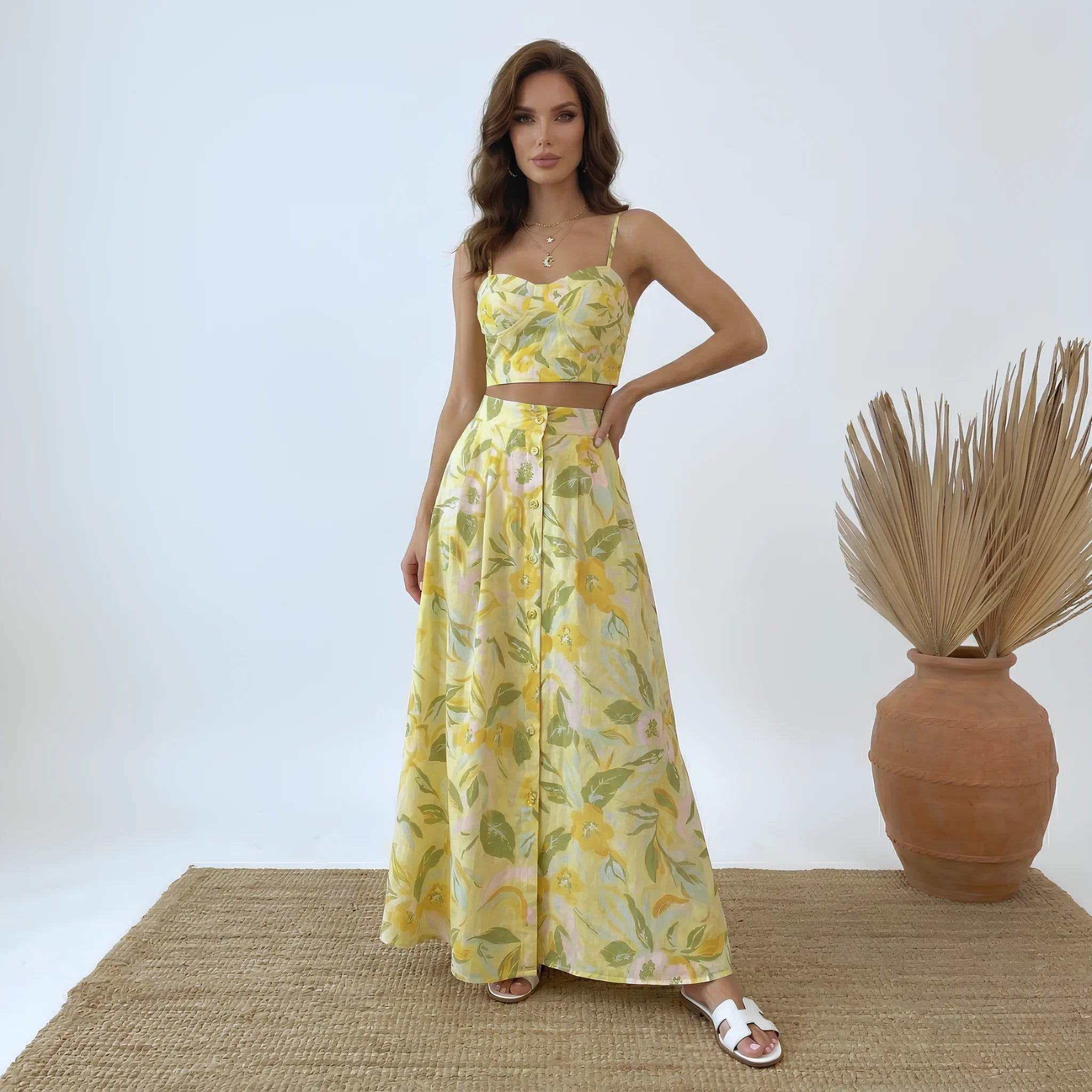 Woman wearing a yellow floral dress standing next to a vase with dried plants on a white background