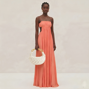 Woman wearing a strapless coral dress holding a white handbag against a plain background