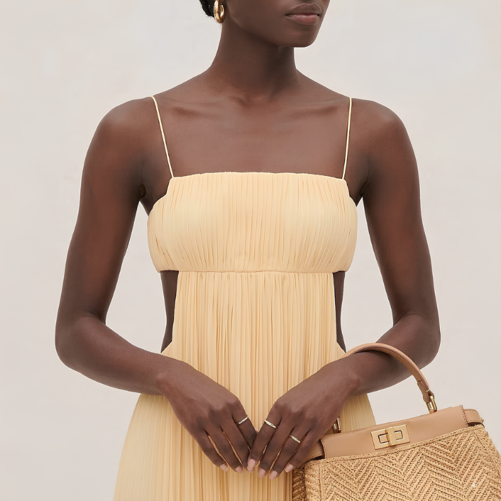 Woman wearing a beige strapless dress holding a matching handbag against a neutral background