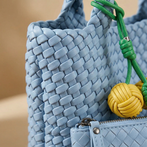 Close-up of a blue woven handbag with a green and yellow decorative element on a beige background