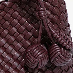 Close-up of a braided brown leather bag with decorative knots.