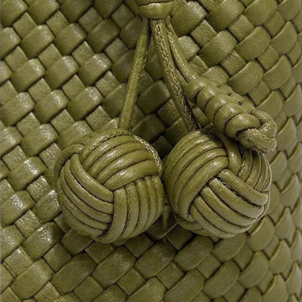 Close-up of a green woven leather bag with knotted handles.