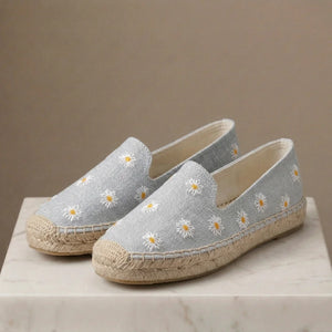 Pair of light blue espadrilles with white floral embroidery on a neutral background