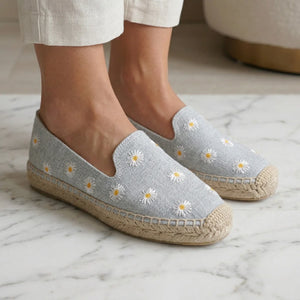 Gray espadrilles with floral embroidery worn indoors on a marble floor.