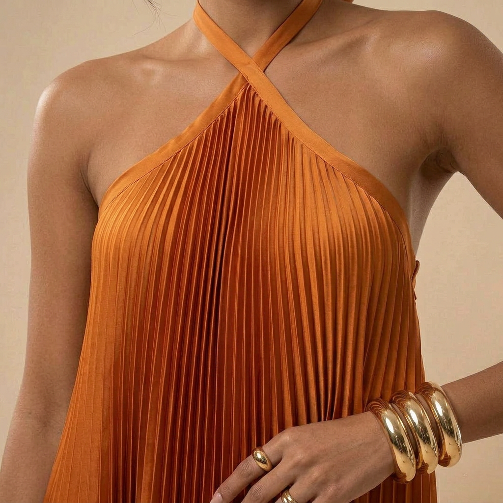 Orange pleated dress worn by a person with gold jewelry on a beige background