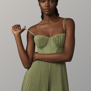 Woman wearing a green pleated dress against a gray background