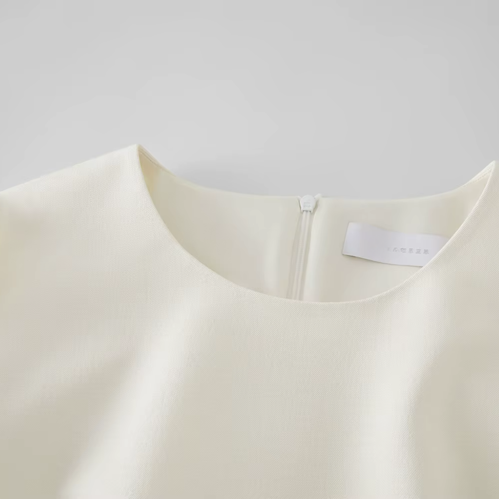 Close-up of a cream-colored garment with a brand label on a light gray background