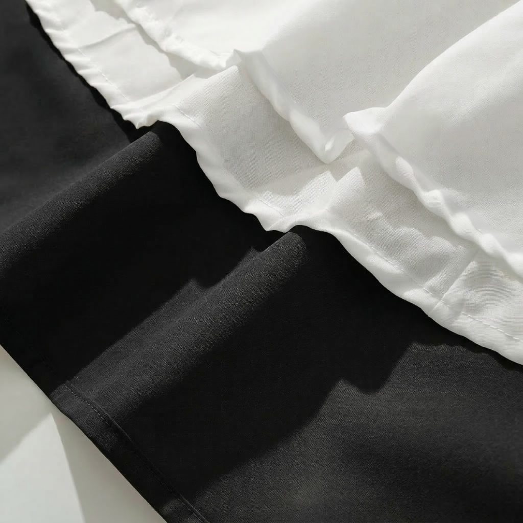 Close-up of black pants with white ruffled trim on a light background