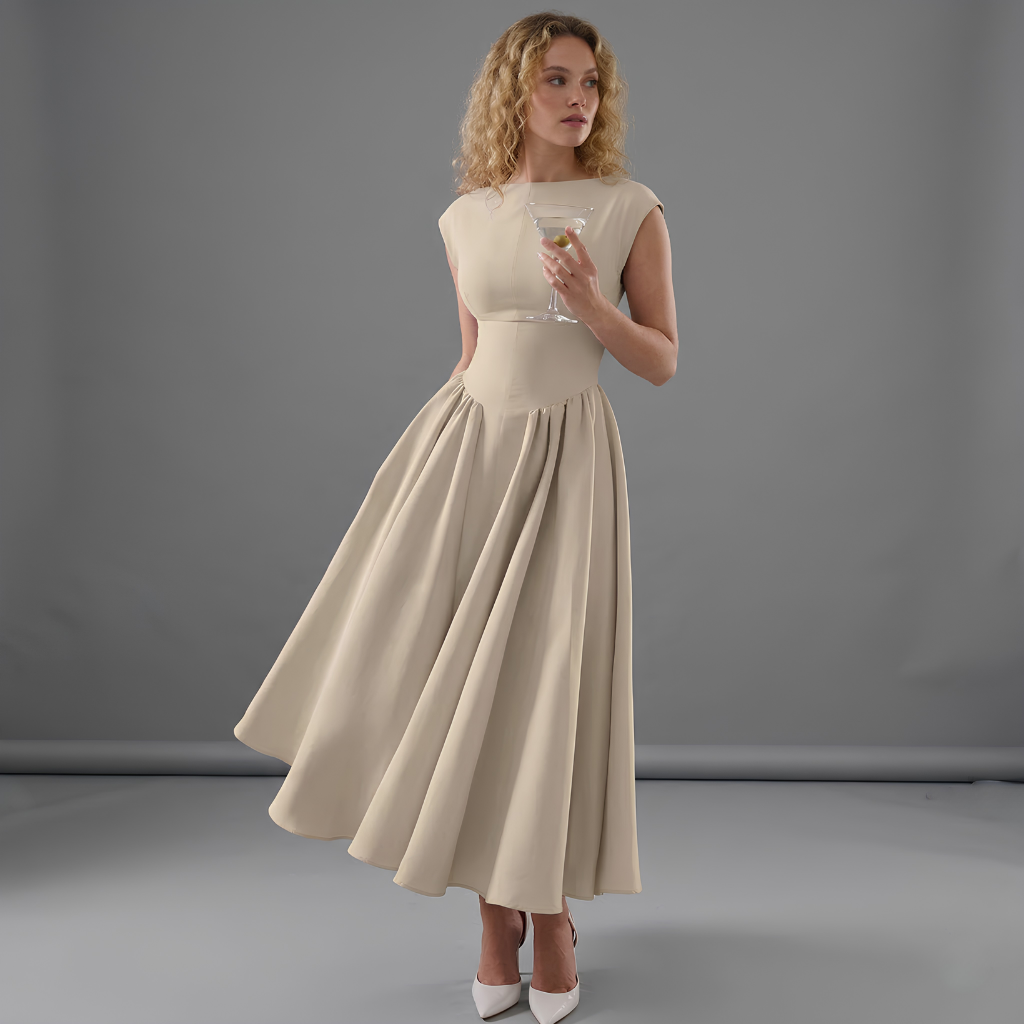 Woman in a beige dress holding a glass against a gray background
