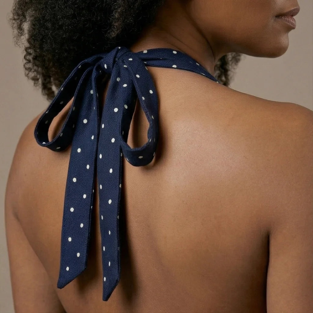Navy blue polka dot scarf tied around a person's neck with a neutral background