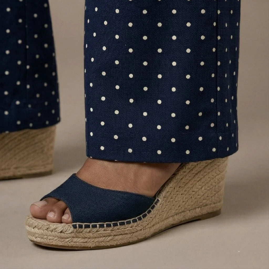 Navy wedge sandal with jute sole worn with navy polka dot pants on a neutral background