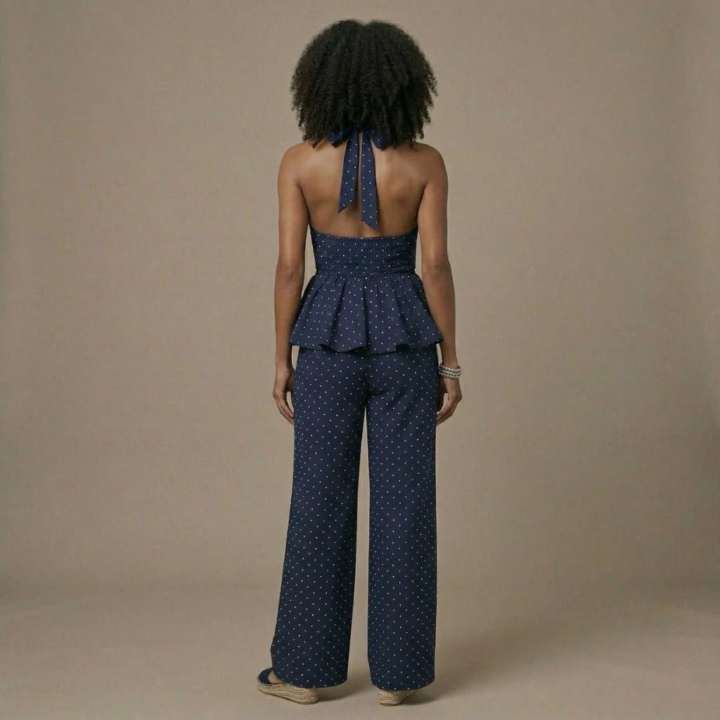 Woman wearing a navy polka dot peplum top and wide-leg pants on a beige background