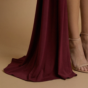 Maroon fabric draped over a person's leg on a beige background